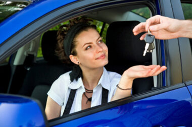 Person sitting in the driver seat of a car holding their hand out to collect the car key held out by the dealer