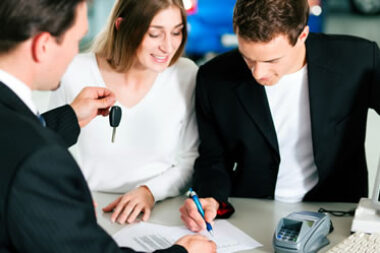 Two people smiling and signing paperwork to purchase a car