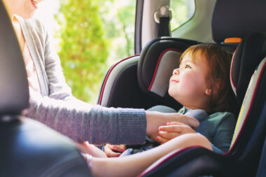 A person putting a child into a car seat in a car