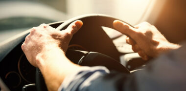 Hands on a steering wheel in the sunshine