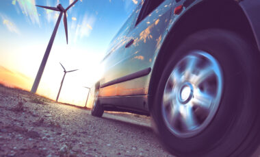 Shot from the ground up of car driving past with wind turbines above it