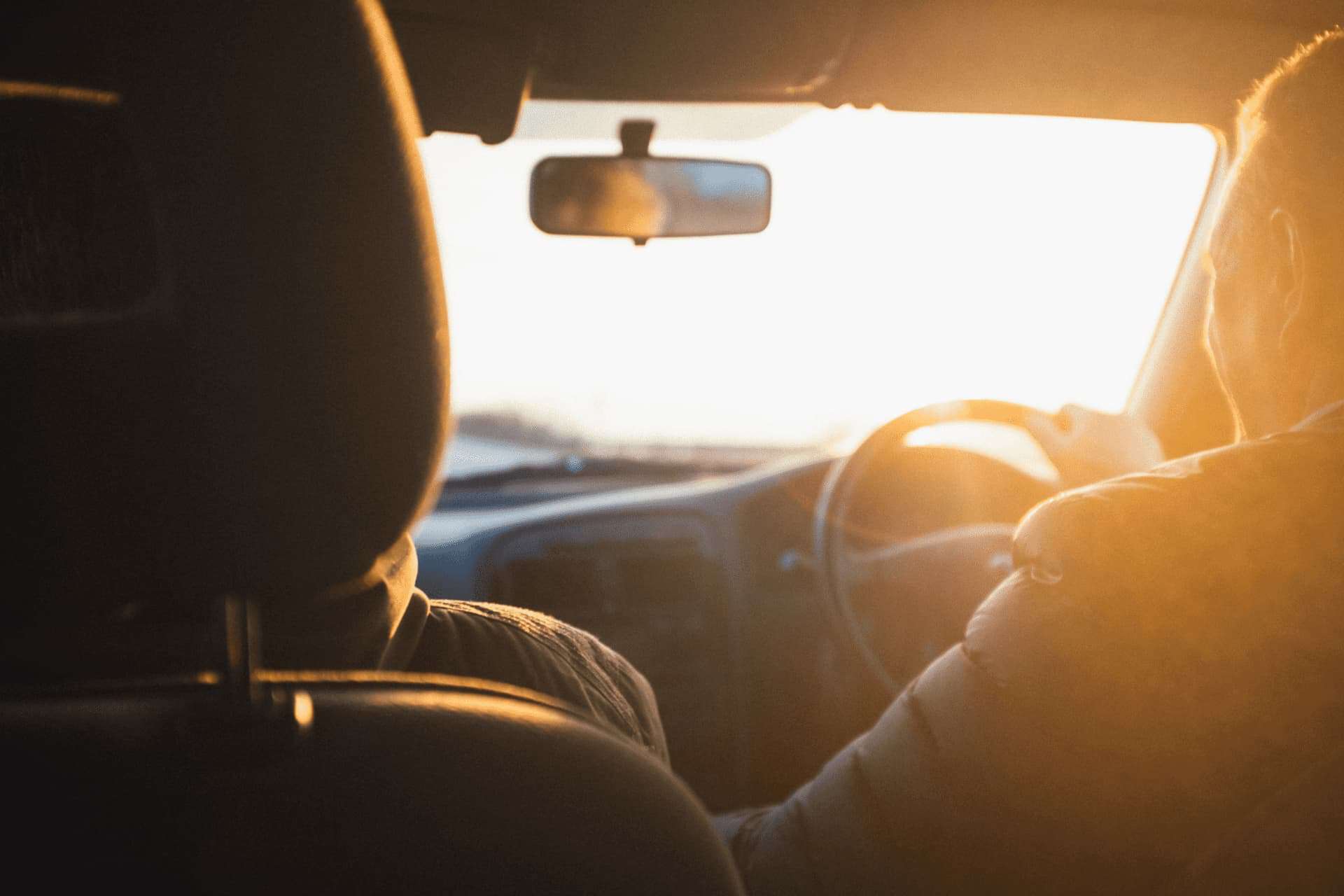 view from back seat of car of someone driving with the sun setting