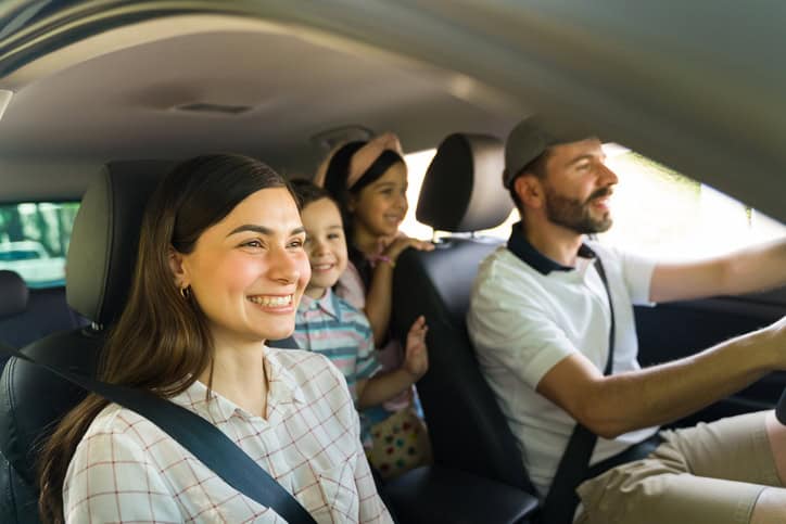 A young family sitting in the car looking ahead at the road smiling