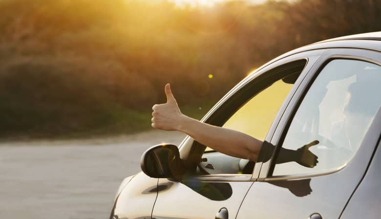 man showing thumbs up from car window at sunset