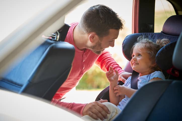 Father securing her daughter into rear child seat before car journey