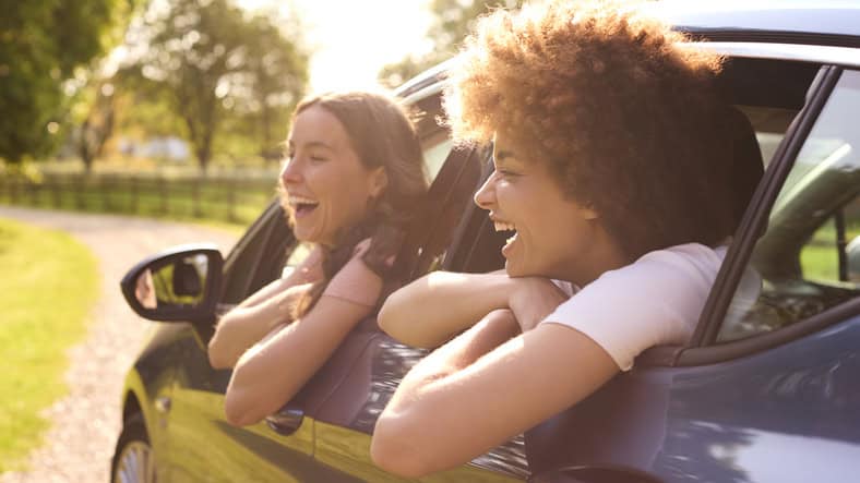 Two Female Friends Or Same Sex Couple In Car On Road Trip Vacation Together Looking Out Of Window